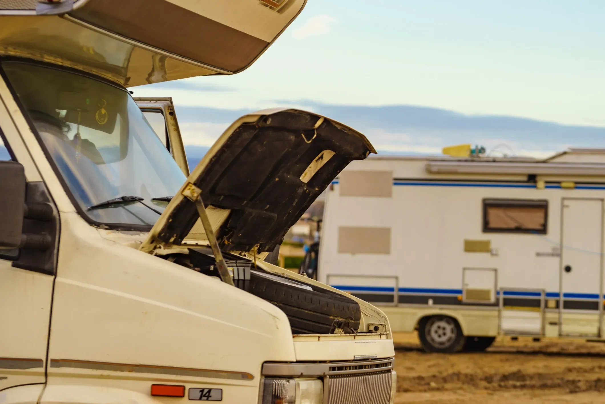 An RV's hood up with another RV in the background. 